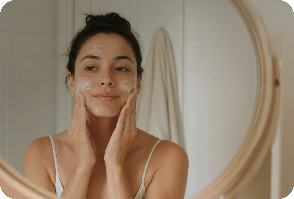 Woman applying cleanser to her face in front of a mirror